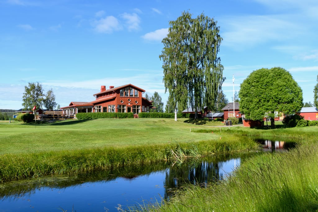 Klubbhuset vid Ljusdals Golfklubb med dammen i förgrunden, sommarbild.